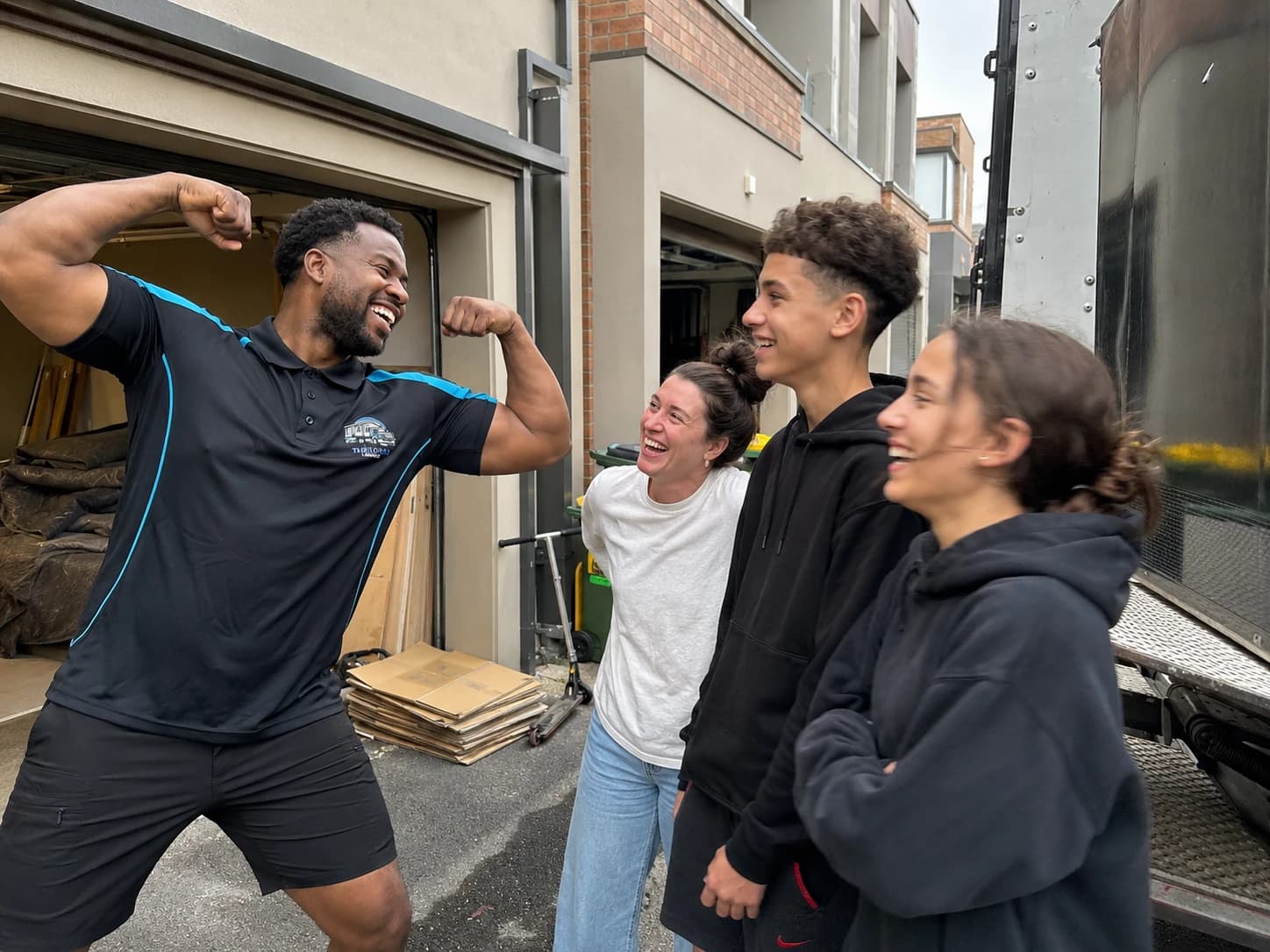 A Load Lounge crew member flexing and laughing with a mother and her two teenagers beside the open truck at the end of their move