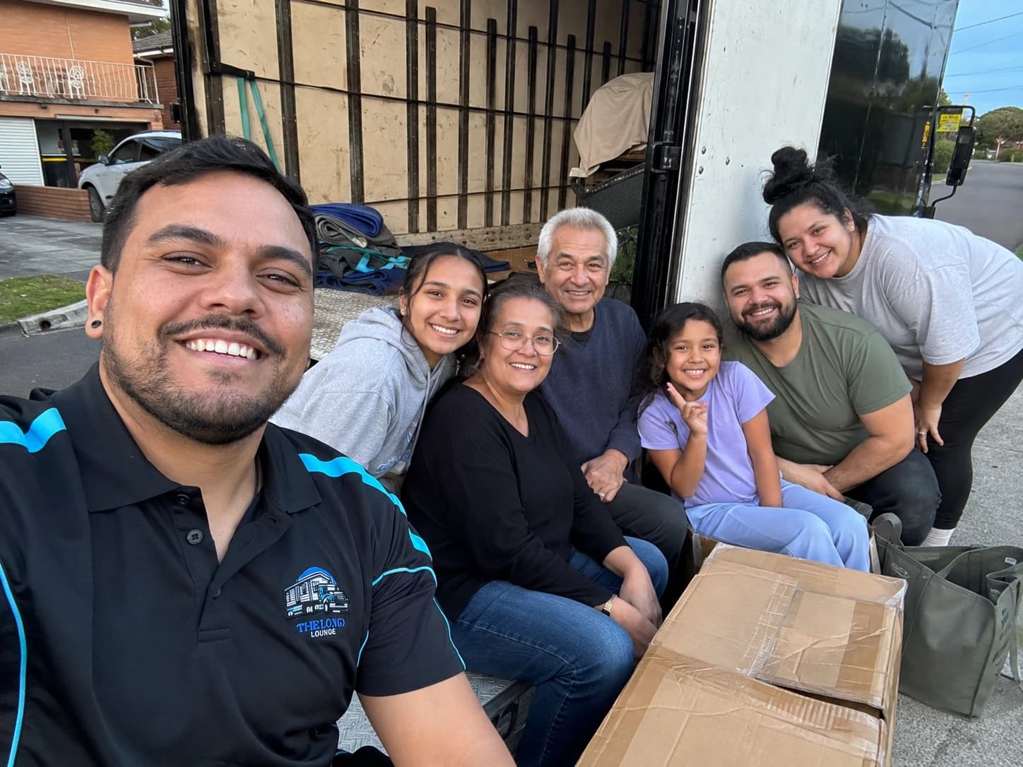 A Load Lounge crew member taking a photo with three generations of a family sitting together on the tailgate of the truck at dusk